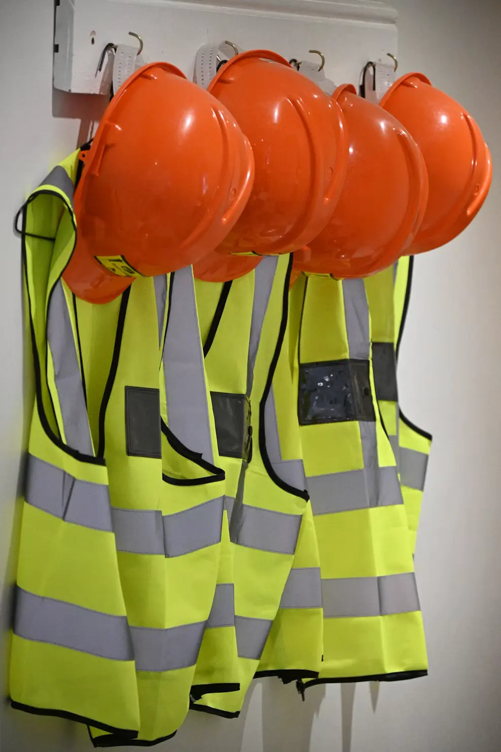 Hard hats and hi-vis vests hanging on a rack.